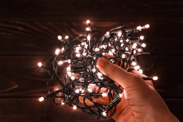 Woman hand holds shining christmas lights garland in a darkness. Glowing LED lightning in a palm. Decorations for winter season holidays Christmas and New Year. Top view.