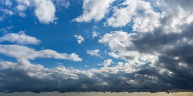 Fırtına geliyormuş. Koyu gri fırtınalı bulutlar parlak mavi gökyüzünü kabarık beyaz bulutlarla kaplıyor. Hava açık güneşliden yağmurlu bulutluya değişiyor. Dramatik bulut manzarası. Hava tahmini, meteoroloji.