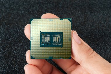 Kadın parmakları, arka planda altın kaplama lensli PC mikro işlemci tutuyor. Modern merkezi işleme ünitesi. Montaj, güncelleme ve tamir için masaüstü bilgisayar donanımı bileşenleri. Makro. Üst görünüm.