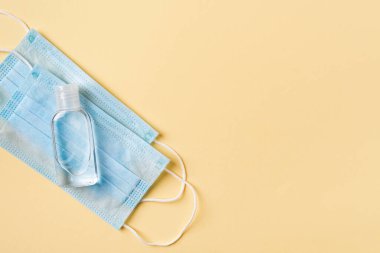 El dezenfektanı küçük bir şişede sarı arka planda tek kullanımlık tıbbi yüz maskeleri. Viral enfeksiyonlara karşı kişisel koruma, covid ve grip. Sağlık hizmetleri. Uzayı metin için kopyala. Üst görünüm.