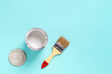 Ahşap saplı boya fırçası ve mavi arka planda beyaz boya kutusu. İnşaat işleri, tadilat ve dekorasyon işleri. Üst görünüm. 