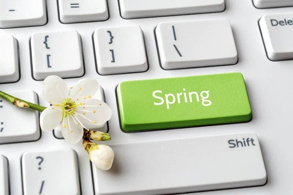 Green key with Spring word and cherry blossom with bud on a white computer keyboard. Spring season mood, holidays and sales concepts. Keypad enter button with message. Top view.