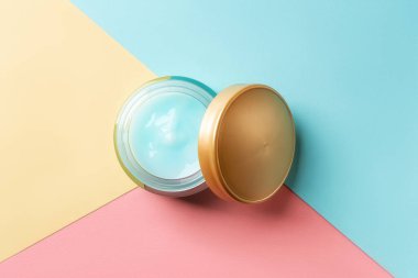 Açık kavanozda nemlendirici yüz jölesi ve mavi pembe kağıdın arka planında altın kapak. Cam kaptaki nemlendirici yüz kremi. Güzellik, cilt bakımı ve kozmetoloji. Sağlık hizmetleri. Üst görünüm.