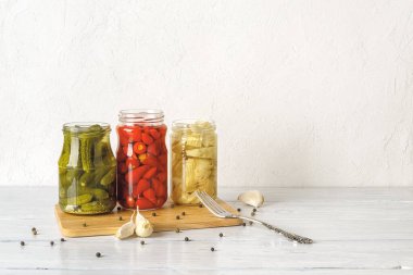 Beyaz ahşap bir masada konserve sebzeli açık cam kavanozlar. Yağlı enginar, turşu turşusu ve küçük kırmızı biber hazır. Mayalanmış organik sebze atıştırmalıkları ve baharatlar. Boşluğu kopyala.