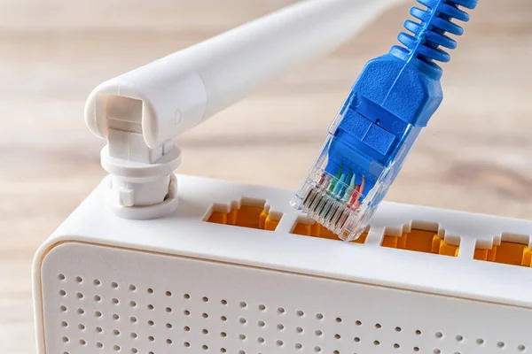 Mavi ağ kablosu kablosuz kablosuz modemi ahşap bir masanın prizine takıyor. Ev ve ofis wlan router 'ı. İnternet donanım makro görüntüsü. Arka görünüm.