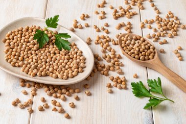 Tabağa kuru fasulye ve beyaz ahşap masa serpiştirilmiş. Sağlıklı vejetaryen gıda konsepti. Humus için ham malzeme. Sebze proteini, karbonhidrat, yağ ve lif kaynağı. Üst görünüm.