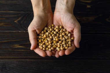 Bir avuç dolusu çiğ nohut ve beyaz bir insan siyah ahşap masa üstünü teslim ediyor. Humus için ham malzeme. Sebze proteini ve lif kaynağı. Sağlıklı vejetaryen yemek tarifi. Üst görünüm.