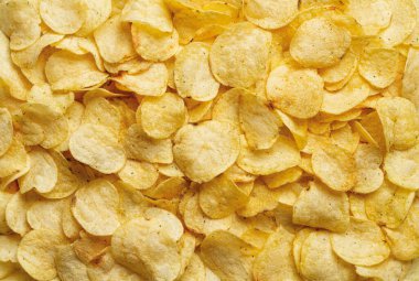 Çıtır patates cipsi. Arka planda dereotu olan lezzetli patates cipsleri. Kızarmış ince dilimlenmiş popüler patates. Cips serpintisi. Sağlıksız yemek ve abur cubur. Tam kare. Üst görünüm.