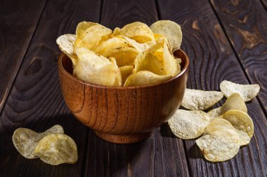Kahverengi ahşap bir kasede, ahşap bir masada dereotlu çıtır organik patates cipsi. Kızarmış patates dilimlerinin çıtır çıtır atıştırması. Fast food, abur cubur ve sağlıksız yemek. Ön görünüm.