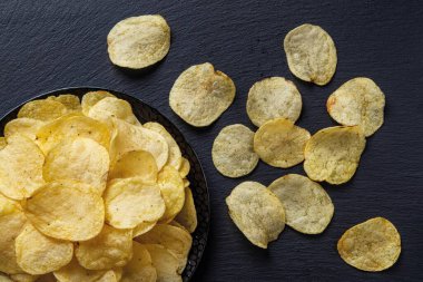 Siyah levha üzerine seramik tabakta patates cipslerinin üst görüntüsü. Lezzetli kızarmış ince patates dilimleri. Fast food, sağlıksız yemek ve abur cubur yemeye hazır. Yakın plan..