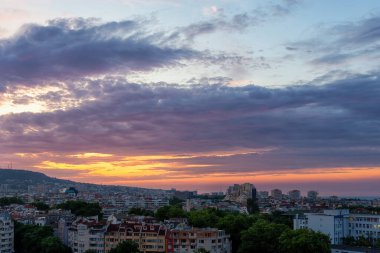 Portakal rengi şafak vakti gökyüzü ve uyuyan şehrin üzerinde mavi renkli bulutlar. Pastel renkli gündoğumu cenneti Varna üzerinde. Sakin bulutlu şafak gökyüzünde parlıyor. Yazın erken saatlerinde şehir manzarası. Tam çerçeve.