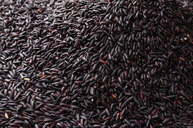 Arkaplan olarak çiğ pirinç yığını. Pişmemiş koyu pirinç yığını dokusu. Vejetaryen diyeti ve sağlıklı beslenme için karmaşık karbonhidratların kaynağı olarak cilalanmamış organik pirinç taneleri. Üst görünüm.