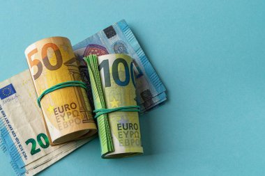 Yeşil rulo 100 avro banknot ve turuncu rulo 50 avro banknot 20 avronun üzerinde kağıt para mavi arka plana karşı. Para saymak, gelir ve harcamalar ve nakit tasarruf kavramları. Uzayı kopyala Üst görünüm.