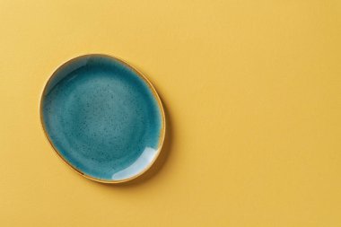 Turkuaz mavisi oval seramik plaka, dokulu sarı arka plan. Modern moda renkli çanak çömlek ve şık yemek tasarımı için sofra takımı. Boş tabaklar. Uzayı kopyala Üst görünüm.