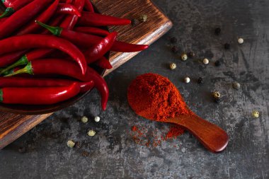 Kesme tahtasındaki kırmızı acı biberli kırmızı kırmızı kırmızı kırmızı biberde ahşap kaşıkta acı biber. Acı biber tozu ve keskin yemekler için acı baharat malzemesi olarak taze taze biber. Gösterişsiz görüntü. Üst görünüm.
