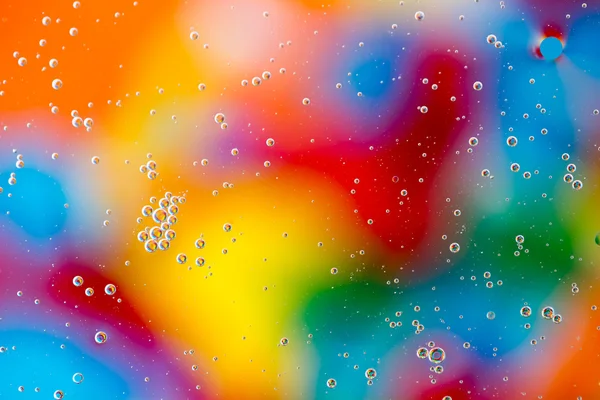 Gotas de aceite en el agua sobre un fondo coloreado — Foto de Stock