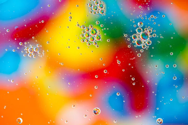 Gotas de aceite en el agua sobre un fondo coloreado — Foto de Stock