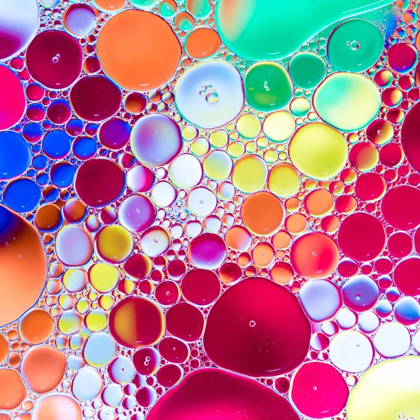 Gotas de óleo na água sobre um fundo colorido — Fotografia de Stock