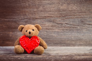 Oyuncak ayı ile eski ahşap arka plan üzerinde oturan kalp.