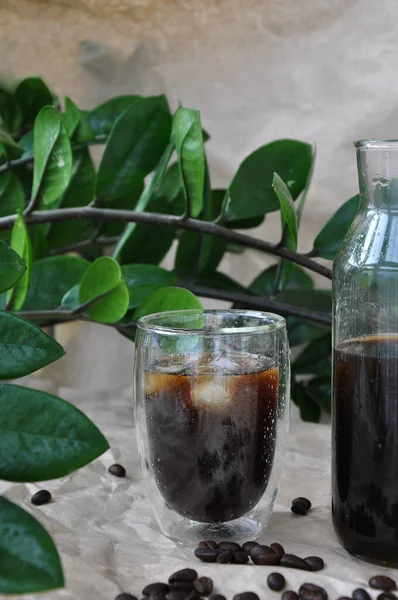 fresh iced black coffee in a glass with coffee beans and green  leaves