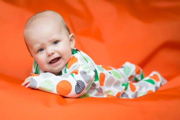 Holčička ležela na břiše na oranžové polštáře — Stock fotografie