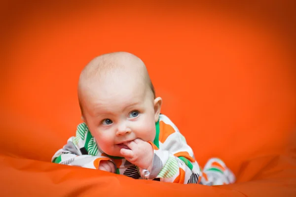 Baby girl lying on a belly on an orange pillow — Stock Photo, Image