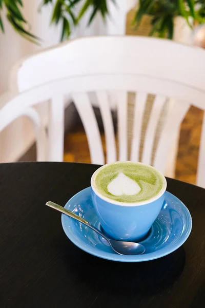 Latte verde matcha en taza azul sobre una mesa negra con silla blanca sobre fondo. Foto vertical tomada en la cafetería —  Fotos de Stock