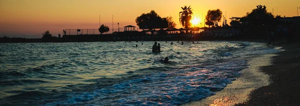 Silhouetten von glücklichen Menschen, die bei Sonnenuntergang im Meer schwimmen und spielen, Konzept über Spaß am Strand — Stockfoto