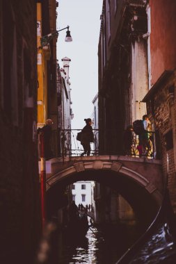 VENICE, İtalya - 27 Ekim 2016: Venedik, İtalya 'daki dar su kanalında eski binalar arasındaki küçük eski köprüdeki insanların silueti