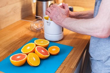 Adam mutfaktaki kırmızı ve turuncu portakallardan meyve suyu sıkıyor.
