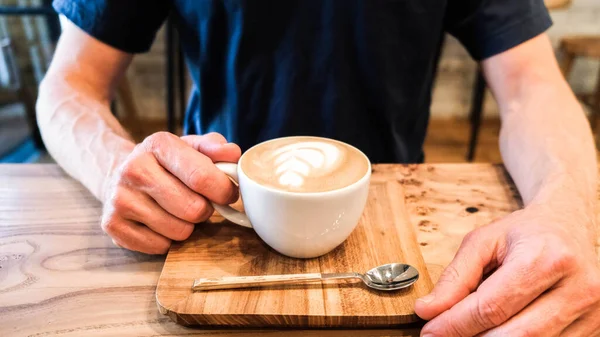 Kobieta ręce trzymać filiżankę kawy cappuccino na kolorowym szklanym stole w kawiarni — Zdjęcie stockowe