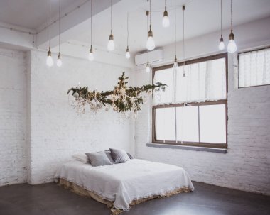 Noel sıcacık kışlık ev dekorasyonu. Noel iç dekorasyonu. Beyaz çarşaflı yatak, battaniye, yastık, battaniye. Tavanda Noel dalları, süslemeler ve LED çelenkler