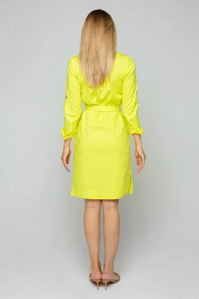 Espalda de hermosa joven posa para la cámara en vestido amarillo aislado sobre fondo blanco —  Fotos de Stock