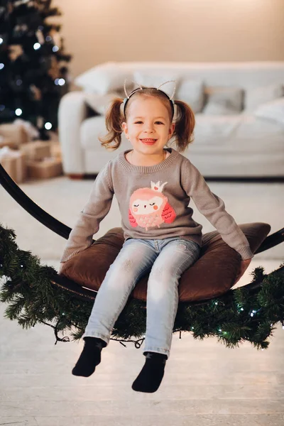 크리스마스 스윙에 사랑 스러운 작은 소녀. 크리스마스 트리. — 스톡 사진
