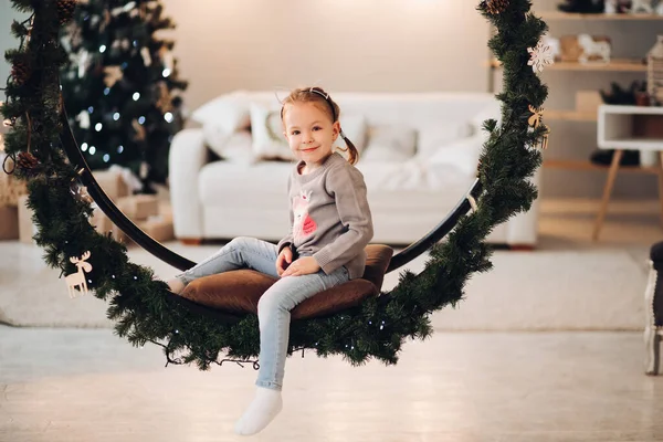 크리스마스 그네에 앉아 있는 예쁜 아이. 크리스마스 트리. — 스톡 사진