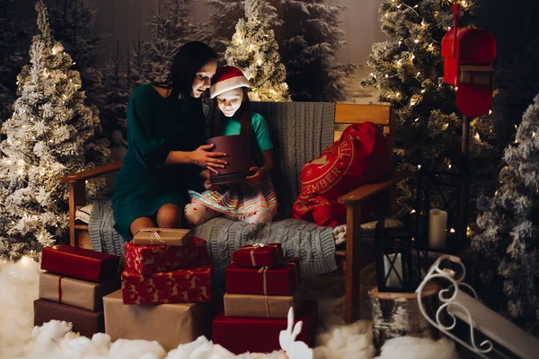 Anne ve kızı Noel hediyelerini açıyor. Bir sürü hediye kutusu ve kardaki köknar ağaçları.. — Stok fotoğraf