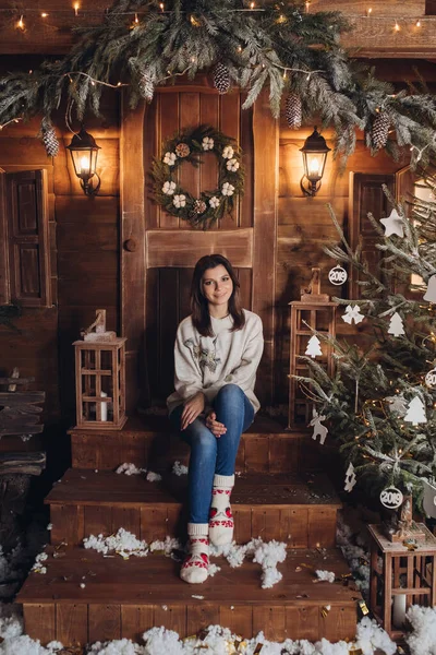Ein junges schönes Mädchen sitzt im gemütlichen Hof eines Dorfhauses, das für das neue Jahr dekoriert ist — Stockfoto