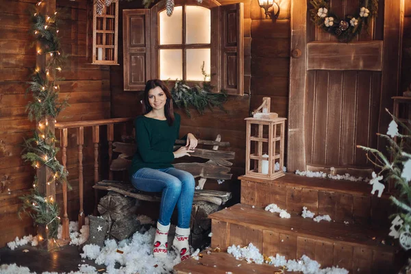 Imagem de uma jovem menina bonita senta-se no quintal acolhedor de uma casa de aldeia decorada para o Ano Novo. — Fotografia de Stock