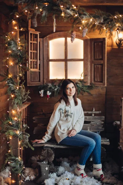 Bild på en ung vacker flicka sitter på den mysiga gården i en by hus dekorerad för det nya året. — Stockfoto