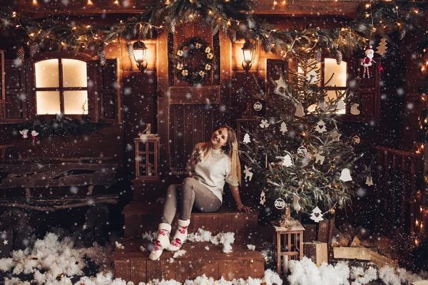 Uma menina bonita jovem senta-se nos degraus perto da casa na aldeia no inverno e sorri — Fotografia de Stock