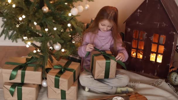 Liten vacker flicka packar upp julklappar på morgonen — Stockvideo