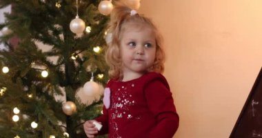 Sevimli küçük bir kız Noel ağacının yanında lezzetli bir şeyler yiyor.