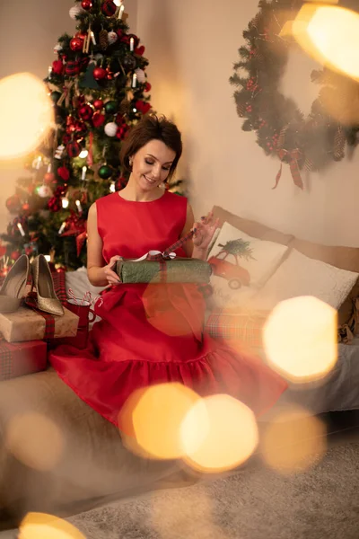 Snygg kvinna i röd klänning tittar på rutan med julklapp — Stockfoto