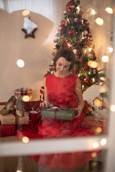 Kırmızı elbiseli çekici kadın Noel hediyesiyle kutuya bakıyor. — Stok fotoğraf