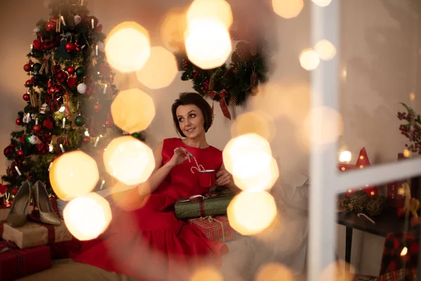 Attraktiv kvinna i röd klänning tittar på rutan med julklapp och tänker på något — Stockfoto