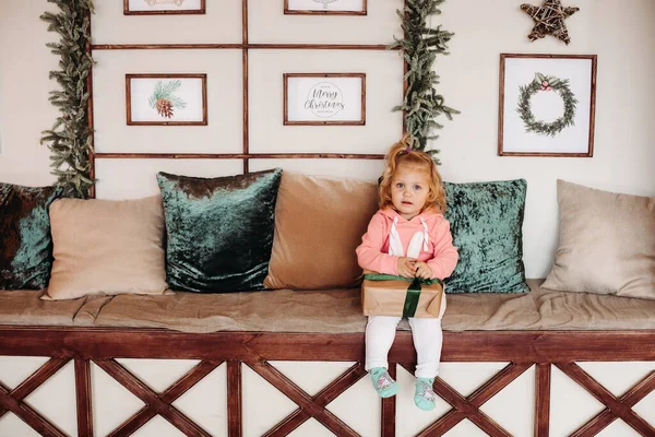 Little pretty girl sith faliste haie siedzi na kanapie z pudełka z prezentem — Zdjęcie stockowe