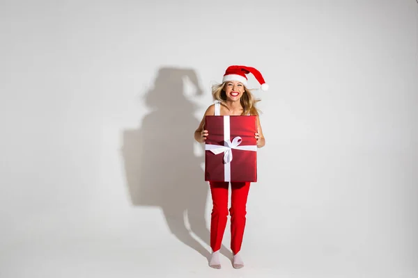 Mulher bonita com chapéu de Natal vermelho e branco detém uma grande caixa com presente e se alegra — Fotografia de Stock