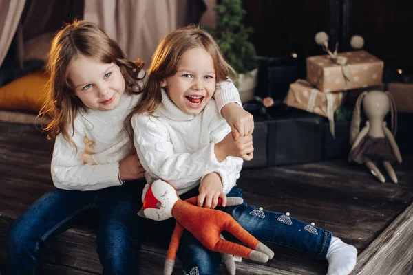 예쁜 자매들은 포옹하고 미소짓습니다. 하얀 뜨개질 스웨터와 청바지를 입고 기쁨에 넘쳐 함께 즐거운 시간을 보내는 소녀들 — 스톡 사진