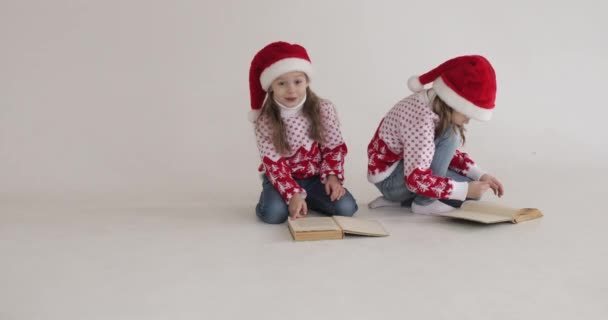 Kleine meisjes in Santa hoedjes lezen boeken. — Stockvideo