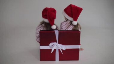 Noel Baba şapkalı iki küçük kız başlarını çeviriyor.